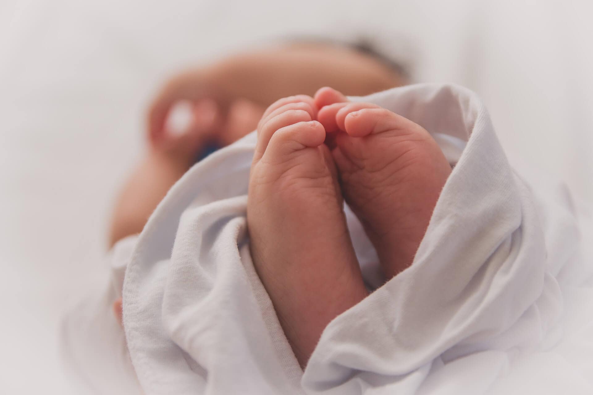 Close-up of a baby's feet wrapped in a white cloth, with the rest of the baby's body blurred in the background.