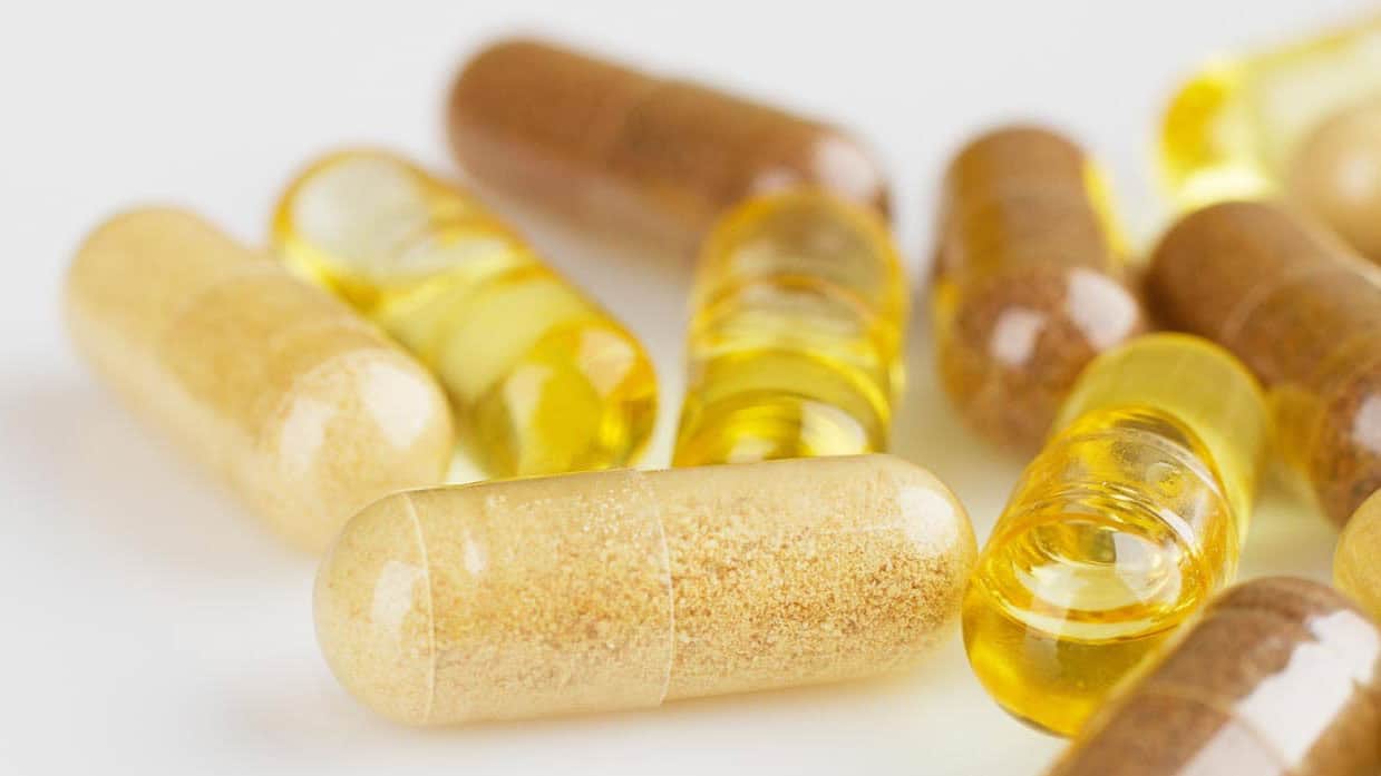 Close-up of assorted capsules and softgel pills in various colors and sizes, placed on a white surface.
