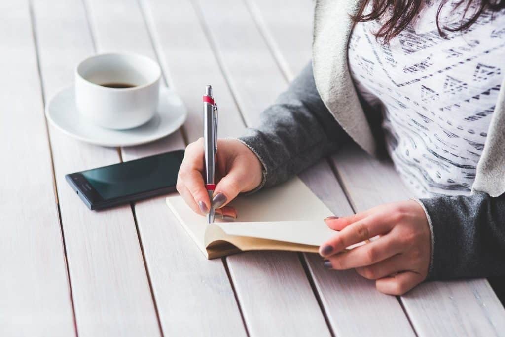 Woman writing in a journal, a cup of coffee by her side.
