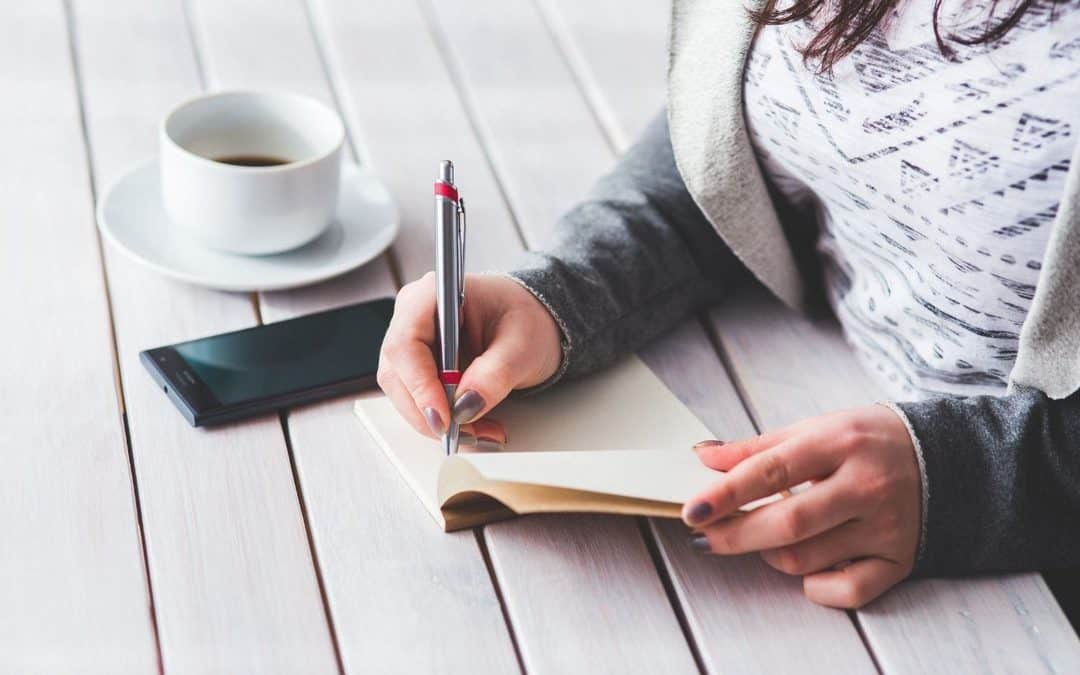 Woman writing in a journal, a cup of coffee by her side.